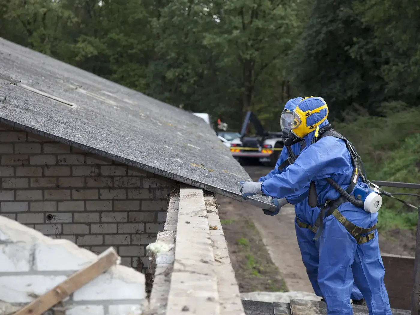 Worker in a powered air respirator hood and protective suit removing roof sheeting