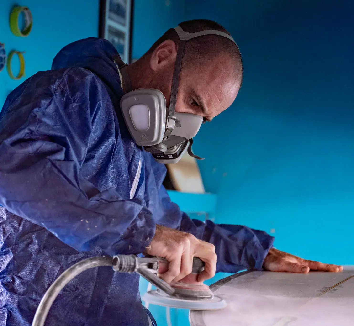 Worker in protective coveralls and a half-face respirator sanding a surface