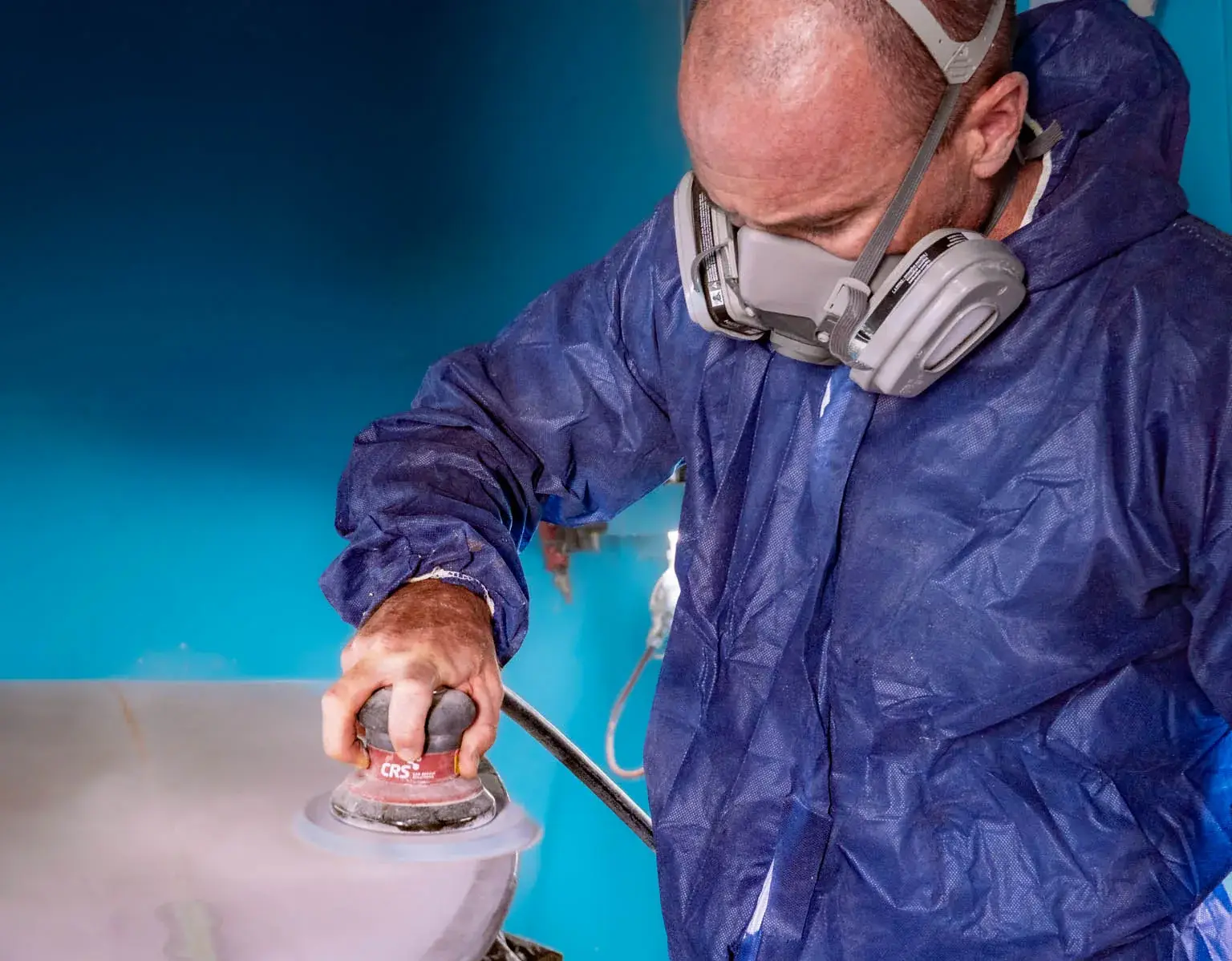 Worker in a protective suit and half-face respirator carrying out abrasive work